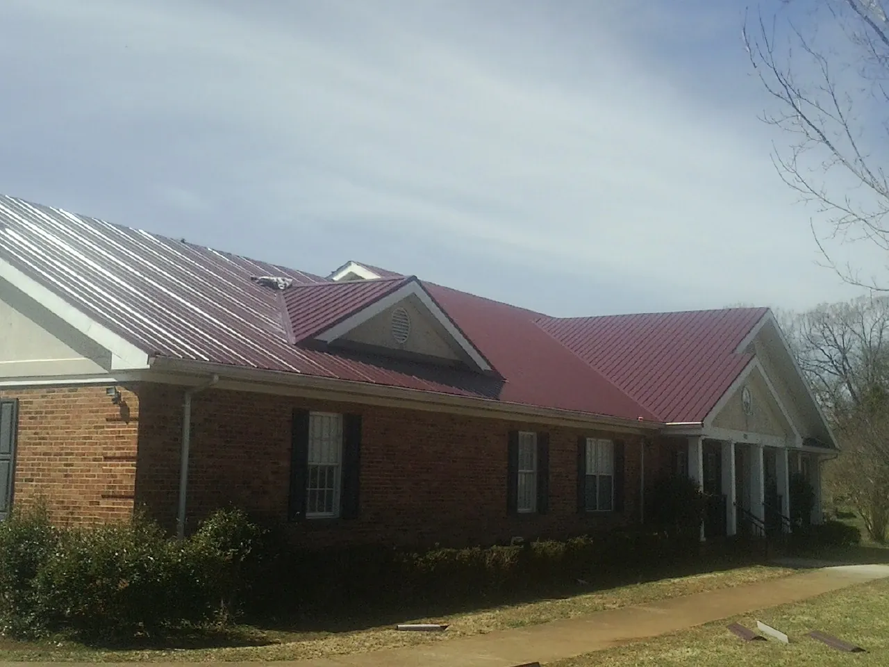 Red metal roof with gabled entries on a long brick building, from a Hail Damage Roof Repair job in Kennedale