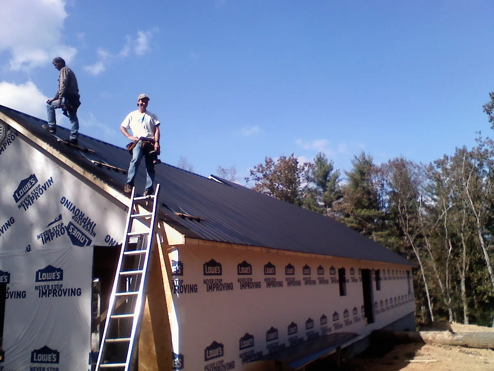 Two roofers standing on a long dark metal roof over a wrapped building in Kennedale